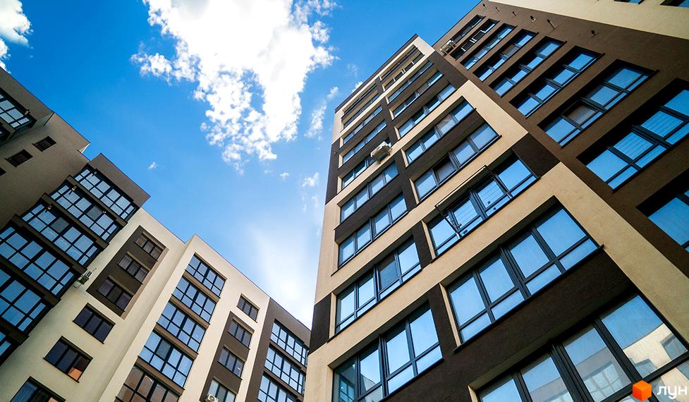 Зображення фасаду та вікон Житлового комплексу Паркова Алея на фоні блакитного неба з хмарами. Вигляд багатоповерхового будинку знизу вгору.