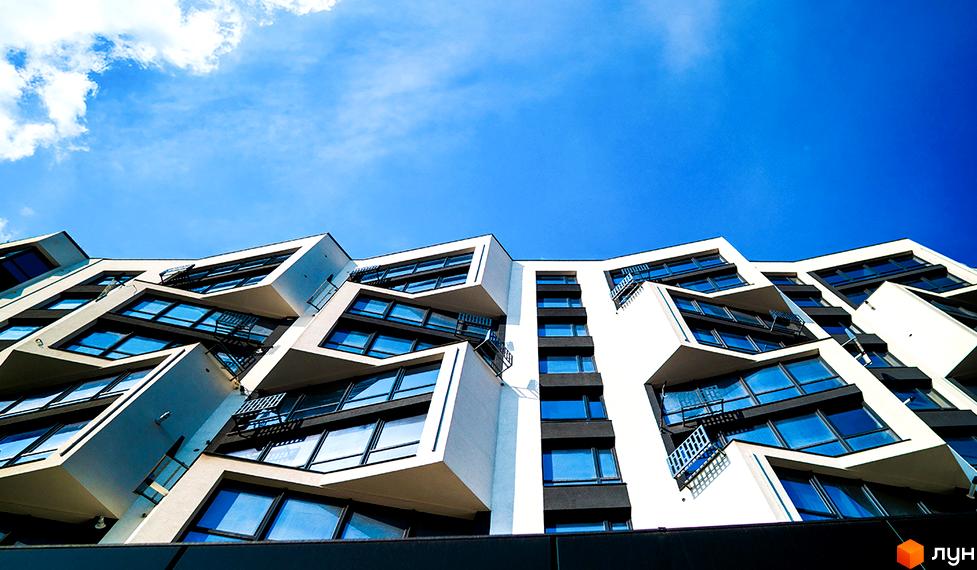 Зображення фасаду будинку Житлового комплексу Паркова Алея з великими вікнами та балконами. Вигляд ззовні на новобудову та блакитне небо.
