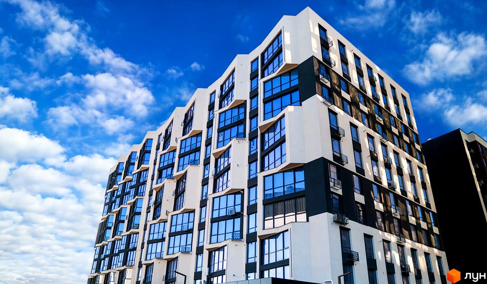 Зображення фасаду багатоповерхового будинку в Житловому комплексі Паркова Алея. На фото видно великі вікна та балкони на фоні блакитного неба.