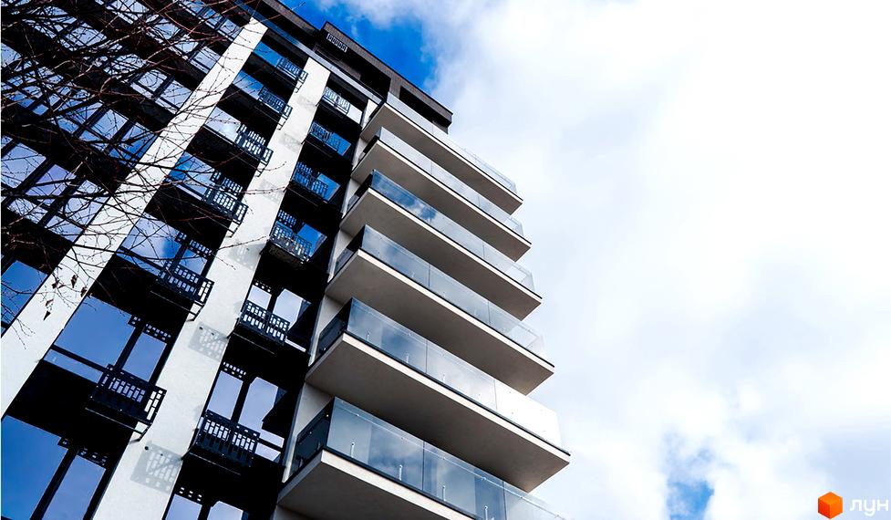 Висотна будівля ЖК Manhattan Up з скляними балконами на фоні блакитного неба. Фасад будинку поєднує білий та чорний кольори, що створює контрастний вигляд.