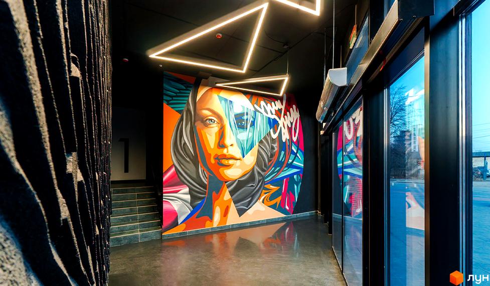 Житловий район Manhattan. Яскраве графіті на стіні вхідної групи. Сучасний дизайн фасаду з великими вікнами та трикутними світильниками.