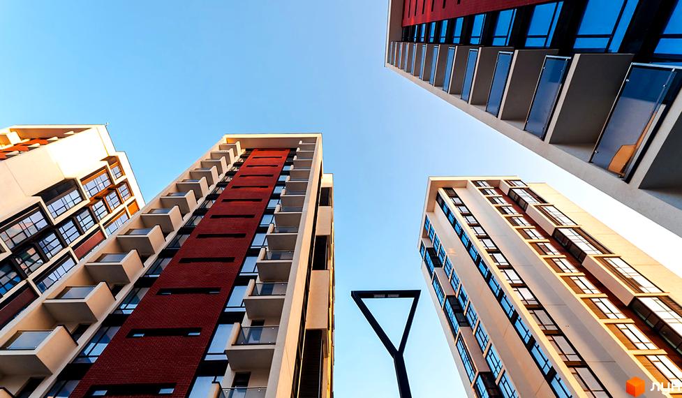 Житловий район Manhattan: сучасні багатоповерхові будинки з червоною цегляною обробкою та скляними балконами на тлі блакитного неба. Комплекс має багато вікон та виступаючих елементів.
