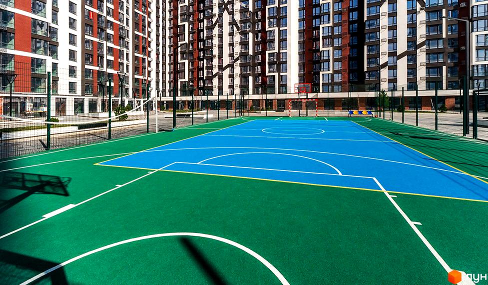 Житловий район Manhattan. Багатоповерховий житловий будинок з червоно-білим фасадом та спортивним майданчиком із синім покриттям та зеленими зонами.