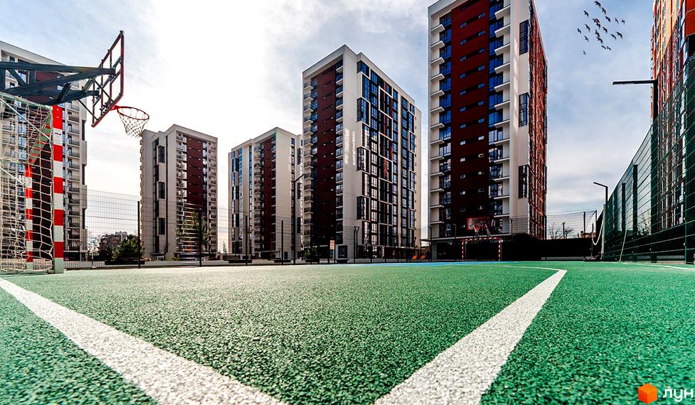 Житловий район Manhattan: сучасні багатоповерхові будинки з червоними та білими фасадами, спортивний майданчик з баскетбольним кільцем та футбольними воротами.