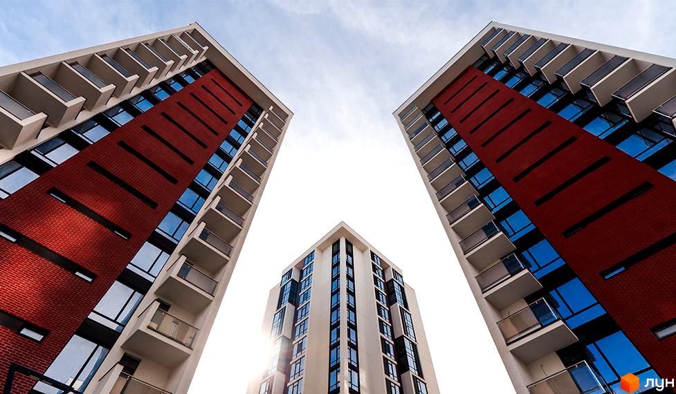 Житловий район Manhattan: три висотні будинки з червоною цегляною облицюванням та скляними балконами на фоні неба. Зовнішній вигляд новобудов.