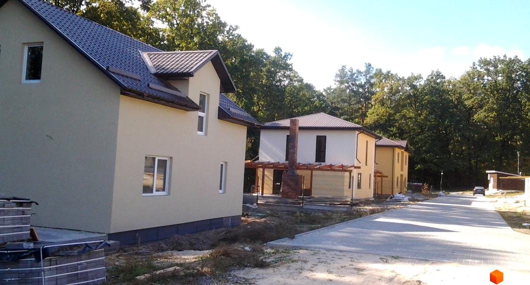 Котеджне містечко Круглик: двоповерхові будинки зі світлими фасадами та темними дахами. Перед будинками прокладена дорога, навколо зелені дерева.