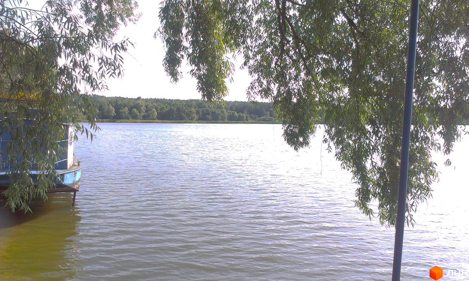 КМ Круглик - котеджне містечко біля озера. Зелені дерева, спокійна водойма та блакитний будиночок на воді створюють мальовничий краєвид.