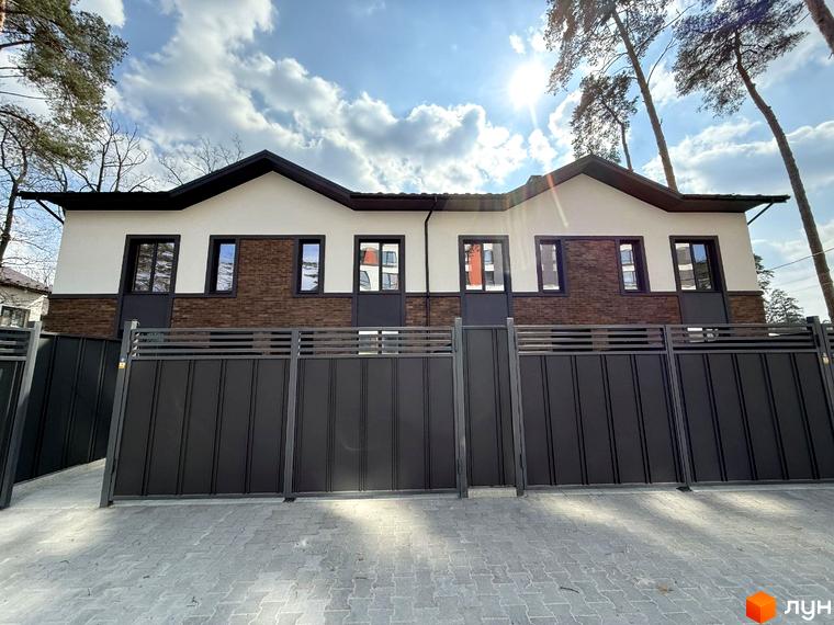 Зовнішній вигляд будинку з коричневою цеглою та білими стінами. На передньому плані сіра огорожа та тротуарна плитка.