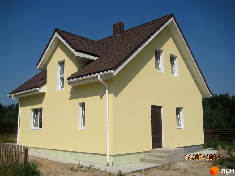 Котеджне містечко Круглик: жовтий двоповерховий будинок з коричневим дахом та білими вікнами. Навколо будинку видно зелені насадження та паркан.