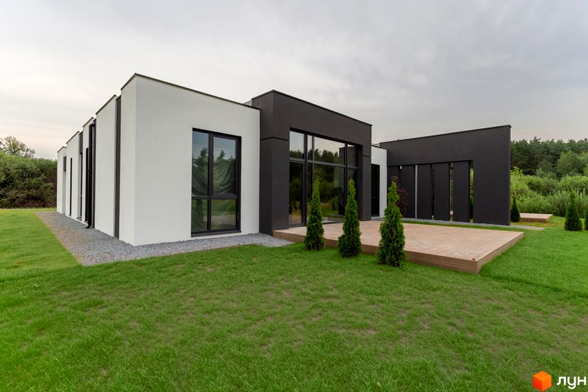 Зображення Duplex Comfort House. Двоповерховий будинок з великими вікнами та дерев'яною терасою, навколо зелений газон і дерева.
