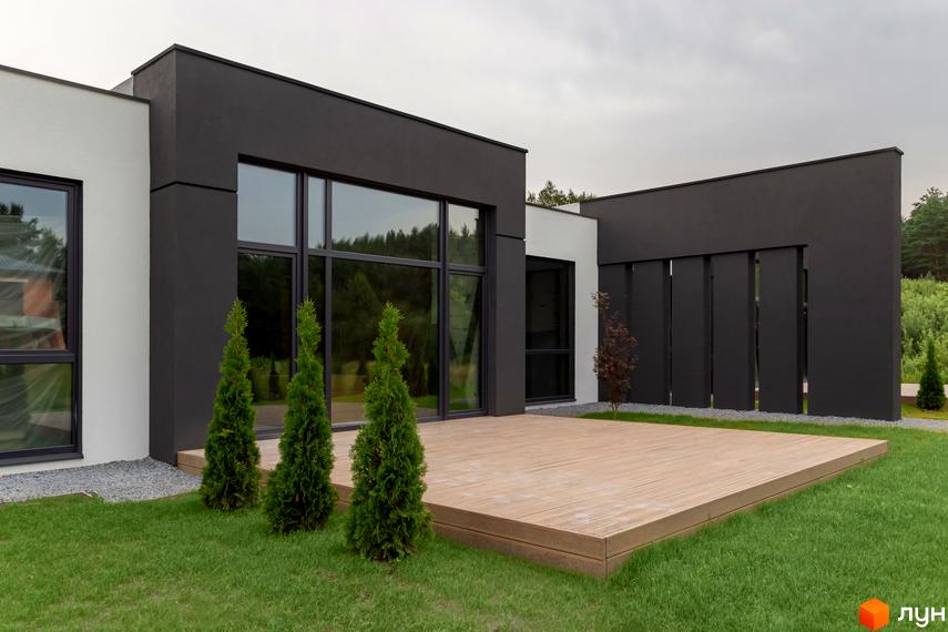 Зовнішній вигляд Duplex Comfort House з великими вікнами та терасою. Навколо будинку зелений газон і декоративні дерева.