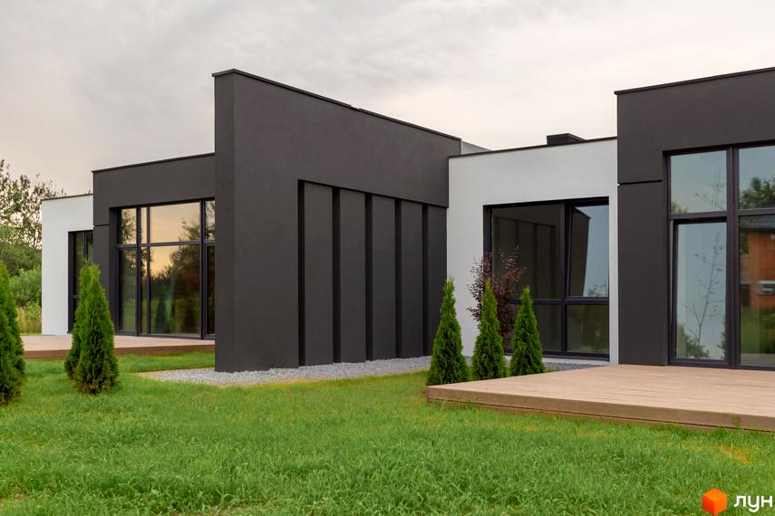 Зовнішній вигляд Duplex Comfort House з великими вікнами та дерев'яним майданчиком. Навколо будинку зелений газон та декоративні дерева.