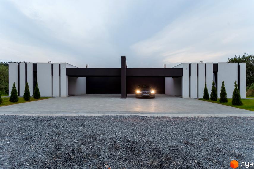 Зовнішній вигляд Duplex Comfort House з гаражем на дві автівки. Перед будинком розташована ділянка з гравієм та невеликі ялинки.