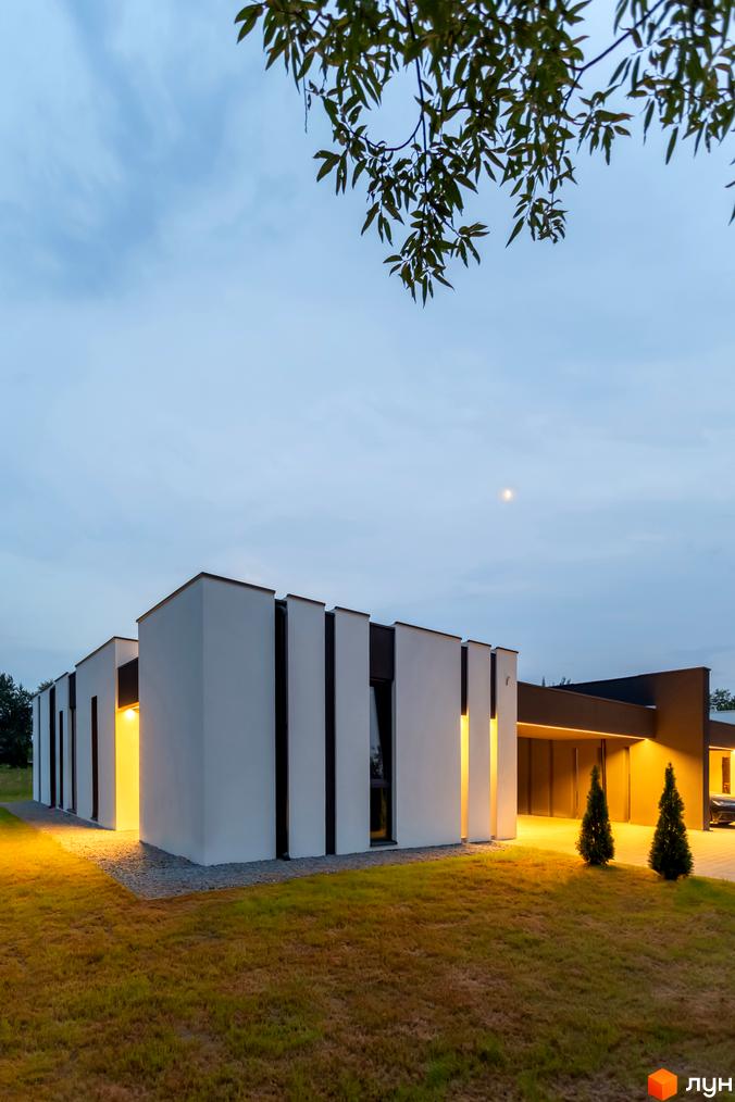 Зображення Duplex Comfort House ззовні. Двоповерхова будівля з білими стінами та чорними вставками, освітлена жовтим світлом.