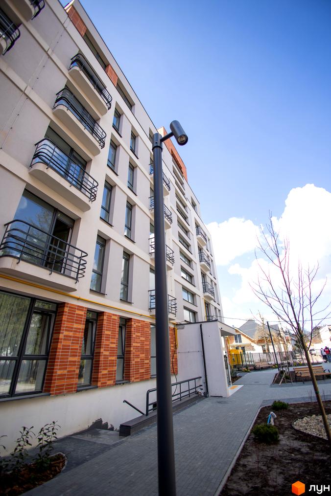 Фасад житлового комплексу РЕМ з балконами та вікнами, прибудинкова територія з доріжками та зеленими насадженнями.