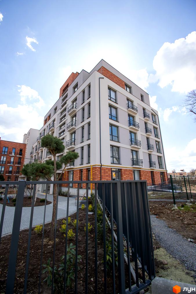 Житловий комплекс РЕМ: багатоповерховий будинок зі світлим фасадом, цегляними елементами та балконами. Облаштована прибудинкова територія з деревами.