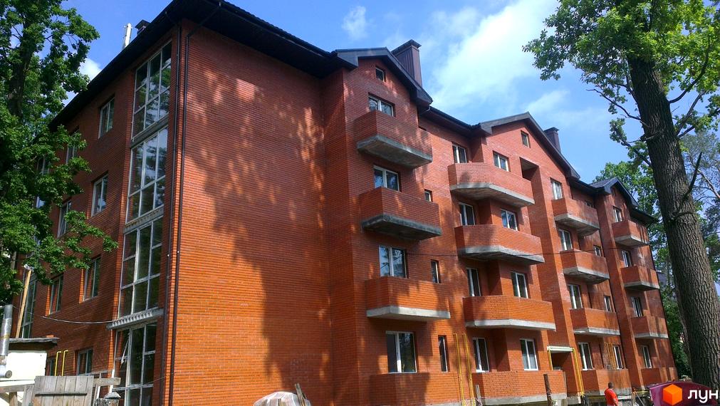 Будинок з червоної цегли житлового комплексу Креатив Хаус має багатоповерхові секції з балконами та великими вікнами. Навколо будівлі ростуть дерева.