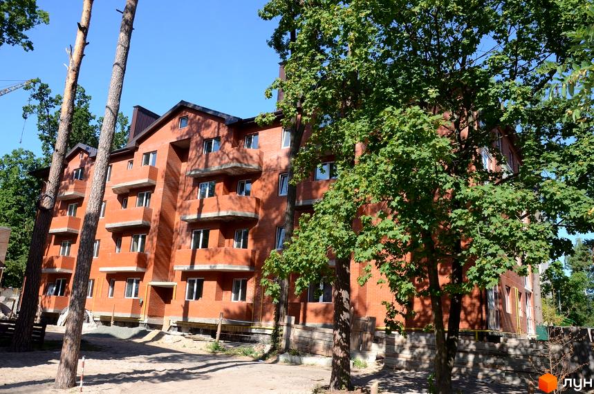 Житловий комплекс Креатив Хаус. Цегляна новобудова з балконами та вікнами, оточена деревами. Територія навколо будинку в піщаній зоні з будматеріалами.