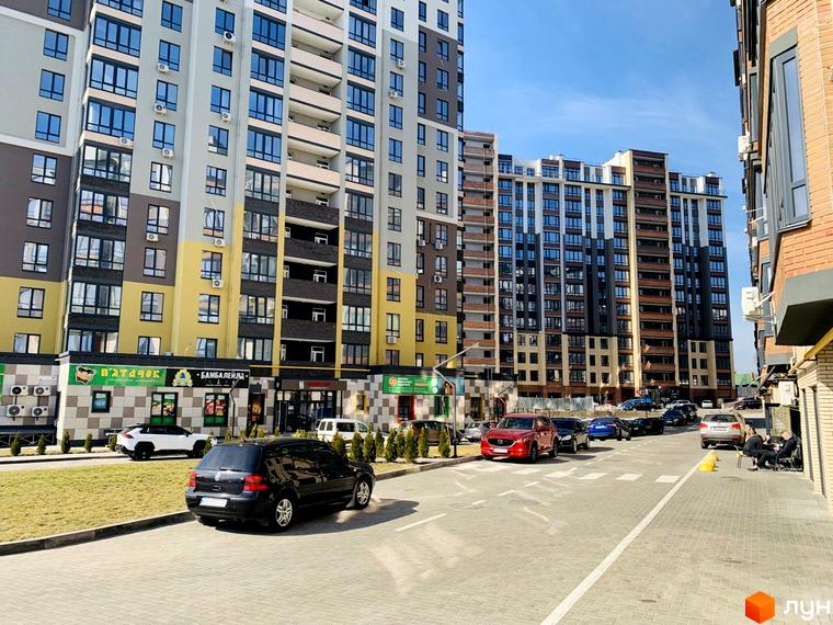 Житловий комплекс Grand City 2 з багатоповерховими будинками, що мають різнокольорові фасади. На прибудинковій території видно проїжджу частину, припарковані автомобілі та зелені насадження.