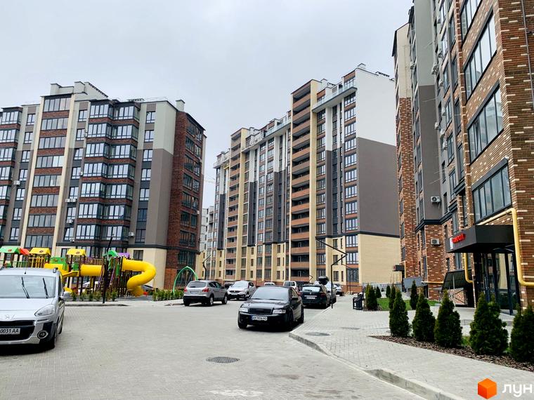 Багатоповерхові будинки житлового комплексу Grand City 2 з цегляними та світлими фасадами. На прибудинковій території розташовані дитячий майданчик та парковка для автомобілів.