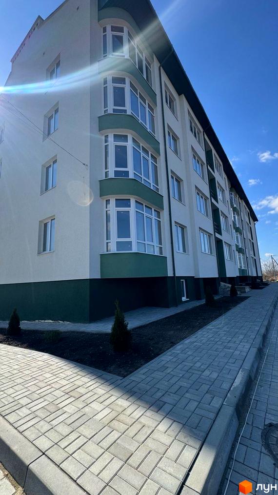 Зображення фасаду багатоповерхового будинку з панорамними вікнами та доглянутою прибудинковою територією з бруківкою. Вид на Житловий комплекс.