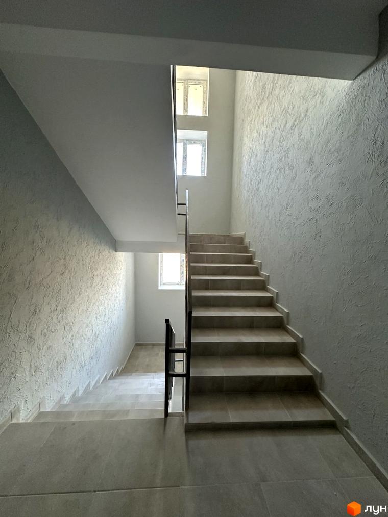 Світлі сходи з плитковим покриттям та текстурованими стінами у під'їзді житлового комплексу на вул. Спортивна.