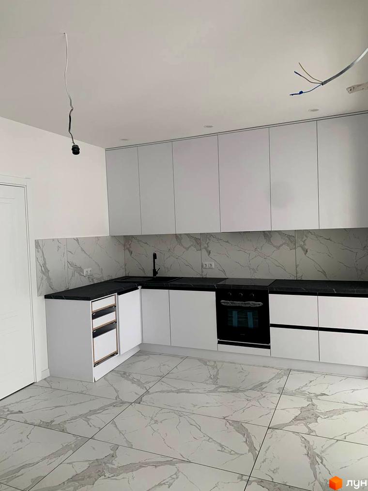 Сучасна кухня з білими фасадами та мармуровим фартухом. Кухонні меблі, плитка та техніка в інтер'єрі новобудови.