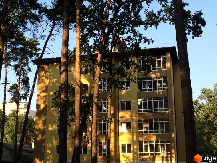 Житловий комплекс Парковий: жовта багатоповерхівка з великими вікнами, оточена високими деревами.