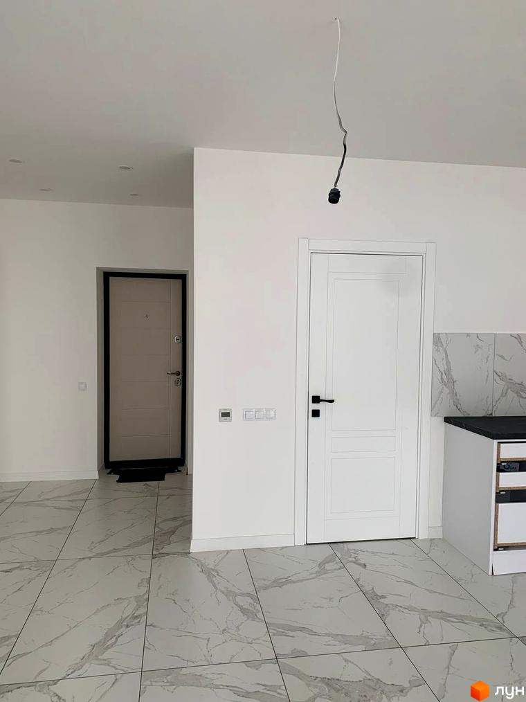 Клубний будинок „На Макіївській“: білі двері, світлі стіни та мармурова плитка на підлозі. Відкритий простір з двома дверима та підвішеним світильником.