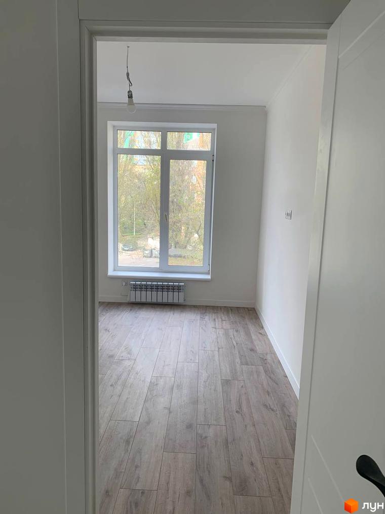 Клубний будинок „На Макіївській“: світла кімната з великим вікном та дерев'яною підлогою, вигляд з прочинених дверей.