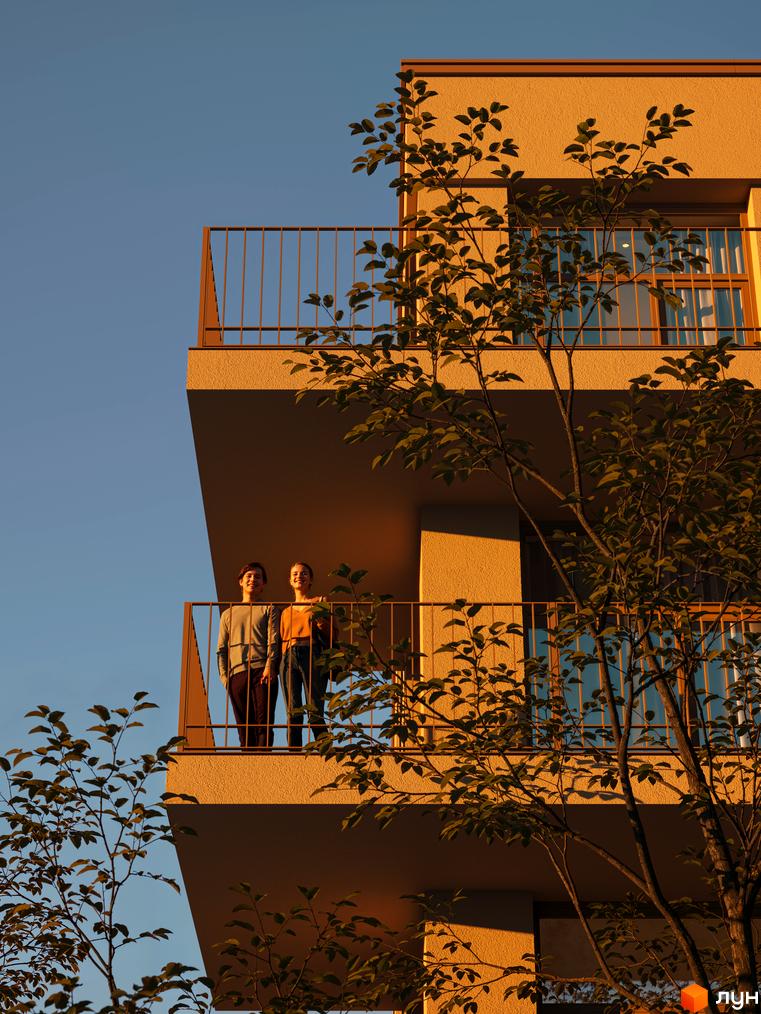 Житловий комплекс Avalon Yard Club: двоє людей на балконі на тлі жовтої стіни будинку та блакитного неба. На передньому плані гілки дерева з листям.