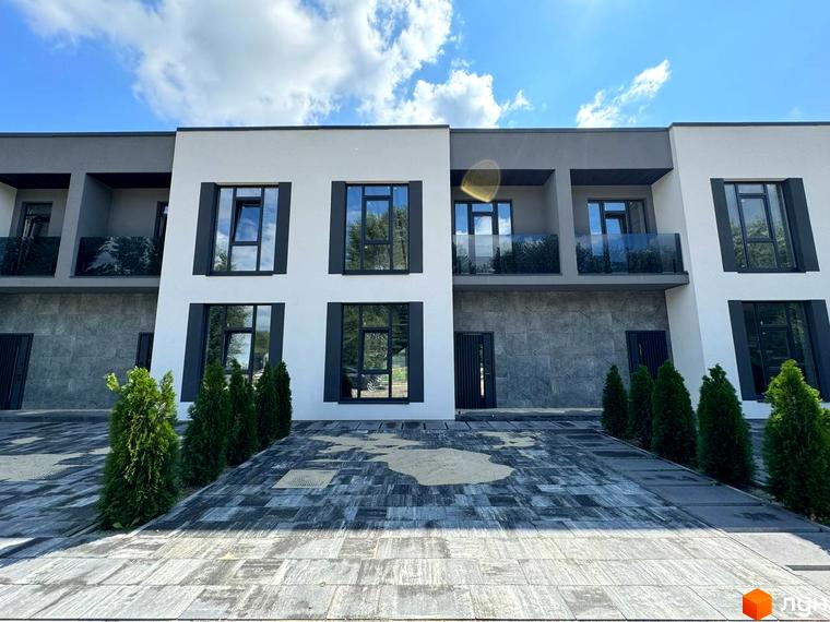 Фасад будинку в житловому комплексі Osocor Apart з великими вікнами та терасами. На передньому плані бруківка та зелені насадження.