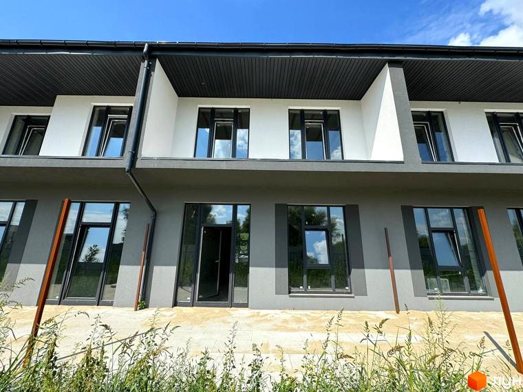 Фасад таунхаусів Osocor Apart, з великими вікнами та терасами, розташованих на тлі блакитного неба. Перед будинками газон з травою та доріжки.