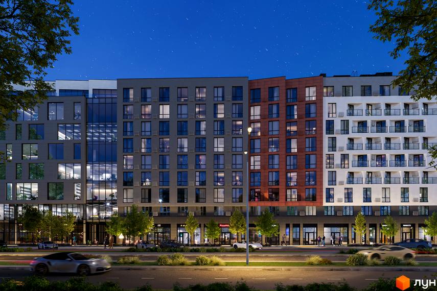 Зовнішній вигляд житлового комплексу Mill Town з фасадами різних кольорів та великою кількістю вікон. Перед будинком розташована дорога з автомобілями та зелені насадження.