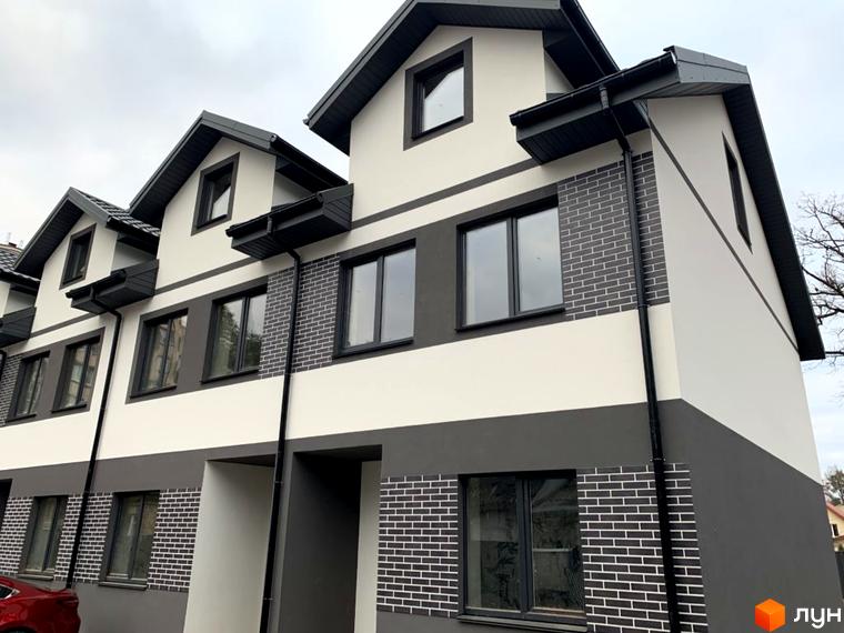 Фасад Таунхаусів „На Котляревського“ має світло-сірі та темно-сірі секції, доповнені вставками з темної цегли. На передньому плані видно частину червоного автомобіля.