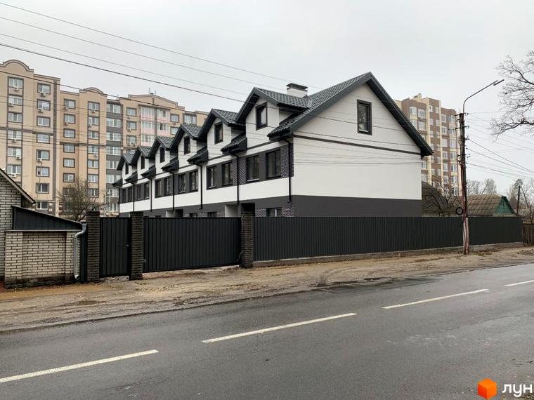 Зображення будинку житлового комплексу Таунхауси „На Котляревського“. Білі стіни, темний дах та паркан. Навкруги будинку асфальтована дорога.