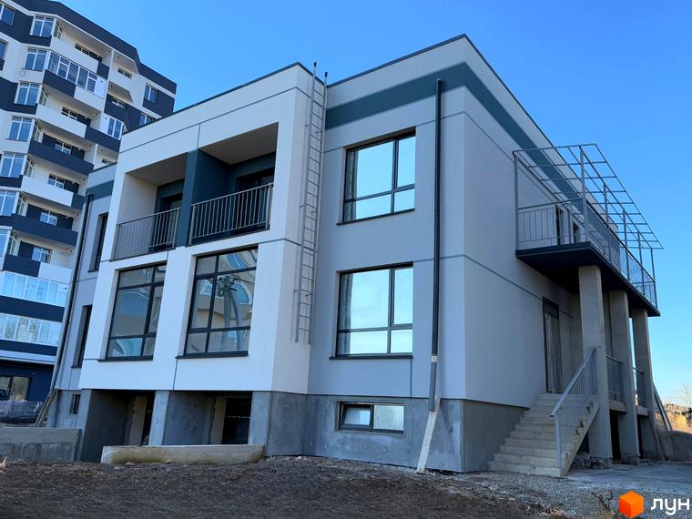 Зовнішній вигляд новобудови 4Family House з балконами та великими вікнами на тлі блакитного неба. Будівельний проєкт з елементами сучасного дизайну.