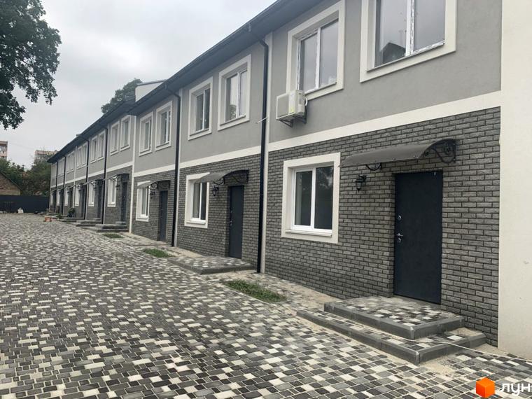 Котеджне містечко Варшавське: ряд двоповерхових будинків з сірими стінами та цегляним оздобленням. Прибудинкова територія вимощена бруківкою.