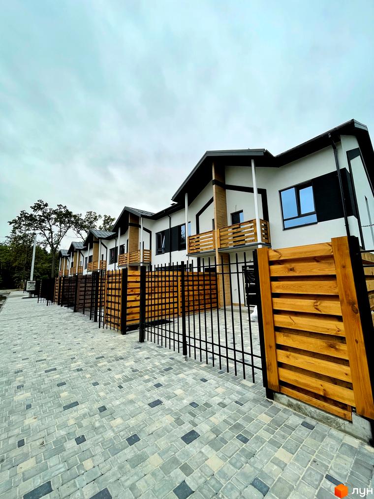 Зображення Котеджного містечка Київське: ряд будинків з біло-чорними фасадами, дерев'яними балконами та огорожею, викладена бруківка.