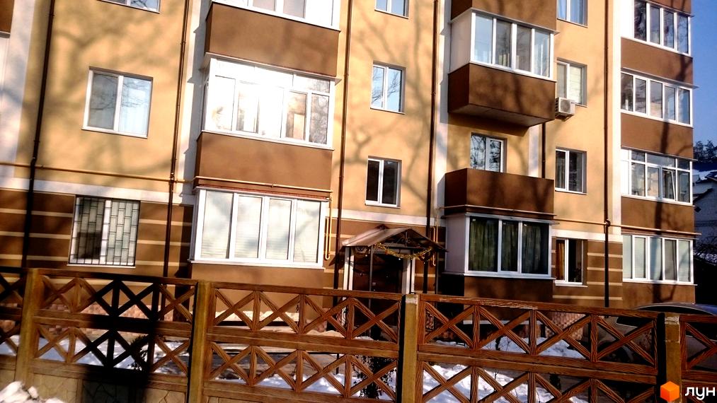 Зовнішній вигляд будинку ЖК Северинівський з коричневими та бежевими фасадами, закритий дерев'яним парканом. Навколо будинку видно дерева та сніг.