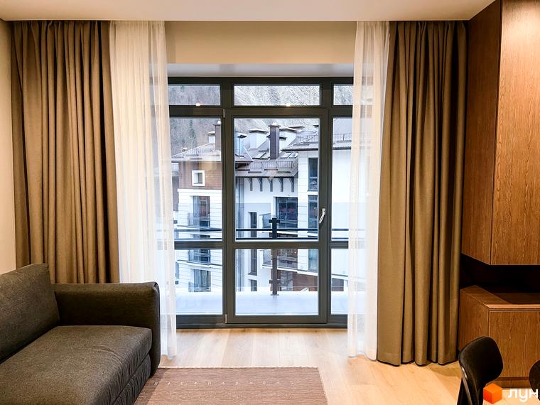 Вікно з видом на будівлі житлового комплексу. Видно засклені балкони та дахи будинків. Красиве планування території.