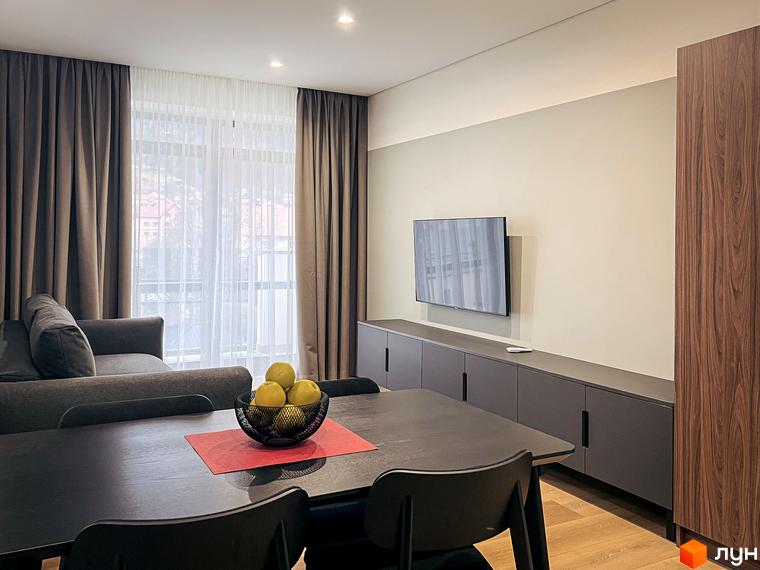 Інтер'єр квартири в апарт-комплексі Крайобраз з великим вікном, телевізором та обіднім столом. Простора квартира з сучасним дизайном.