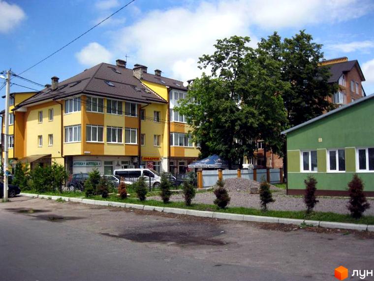 Житловий комплекс на вул. Центральна, 4а. Фасад будівлі жовто-оранжевого кольору з білими вікнами. На прибудинковій території ростуть дерева та кущі.