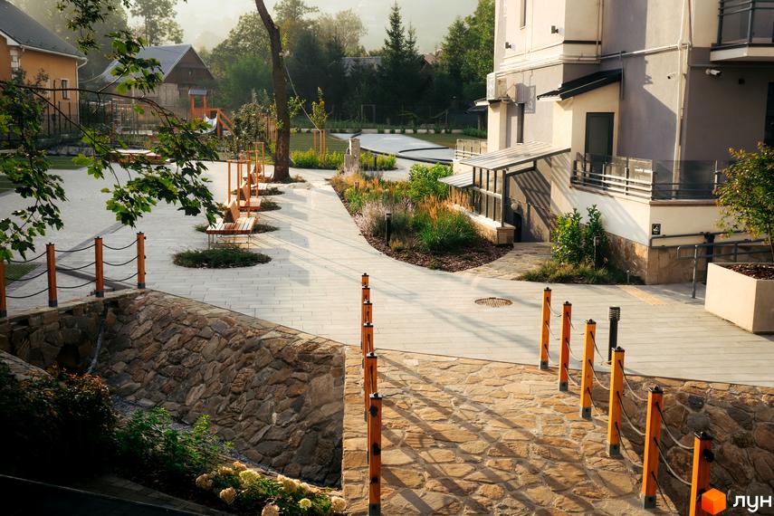 Зображення сторінки житлового комплексу з будівлею з світлою фасадною частиною та доглянутою прибудинковою територією з ландшафтним дизайном.