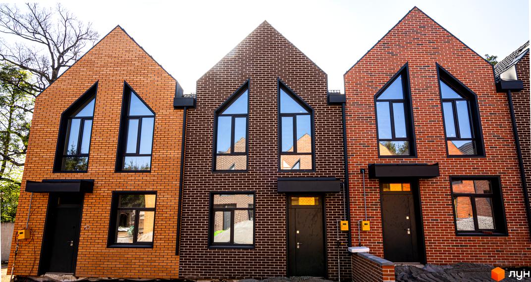 Фасад таунхаусів FORT HOMES з цегли з великими вікнами. Будинки розташовані поруч, на прибудинковій території зелені насадження.