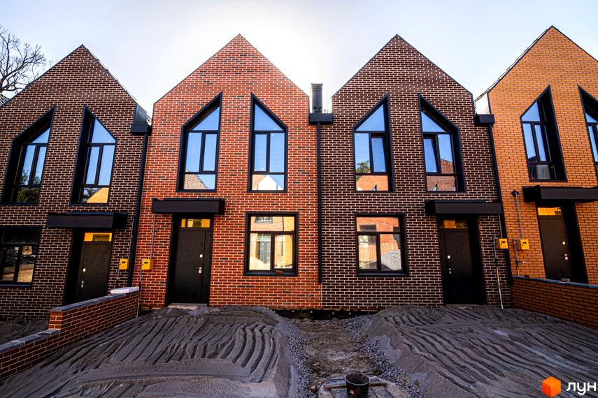 Зображення таунхаусів FORT HOMES з цегли з великими вікнами. Перед будинками насипаний пісок, тривають будівельні роботи.