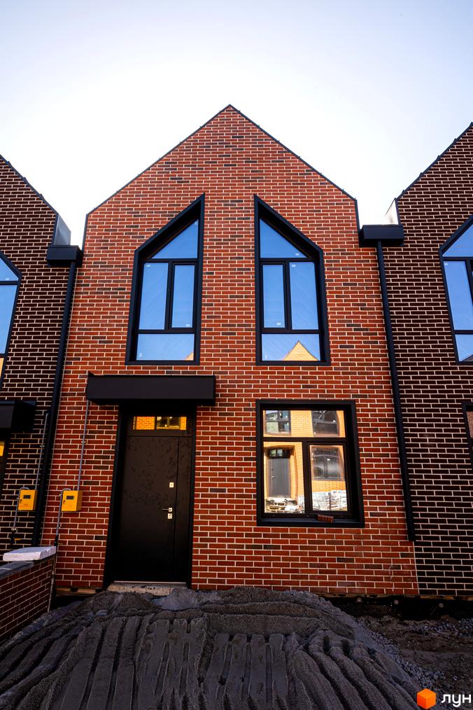 Фасад таунхауса з червоної цегли з великими вікнами у FORT HOMES. Перед будинком видно будівельний майданчик.