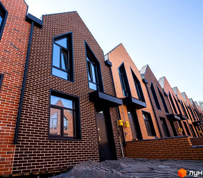 Зображення фасаду таунхаусів FORT HOMES з цегли з великими вікнами. Вигляд на ряд будинків з прибудинковою територією.