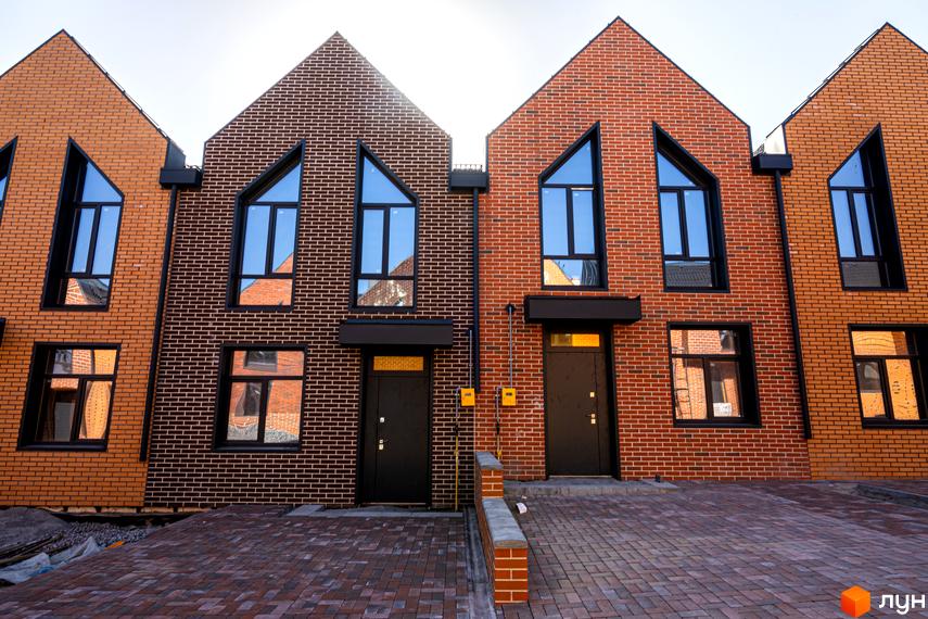 Таунхауси FORT HOMES з червоної та темно-коричневої цегли з незвичними вікнами. Перед будинками вимощена бруківкою територія.
