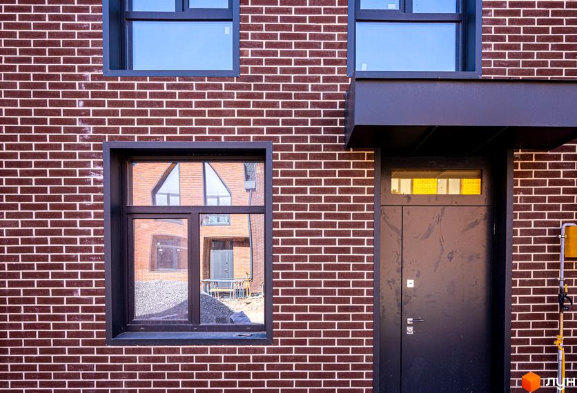 Фасад та вхідна група таунхауса в FORT HOMES. Вікна відображають сусідній будинок та будівельний майданчик.